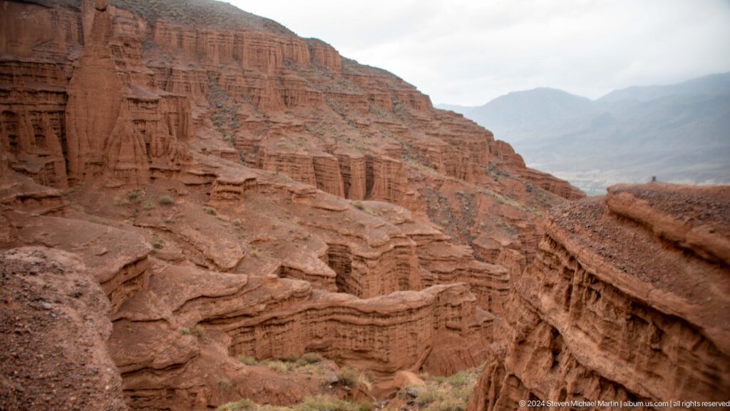 Layered red canyon terraces descending into valley.