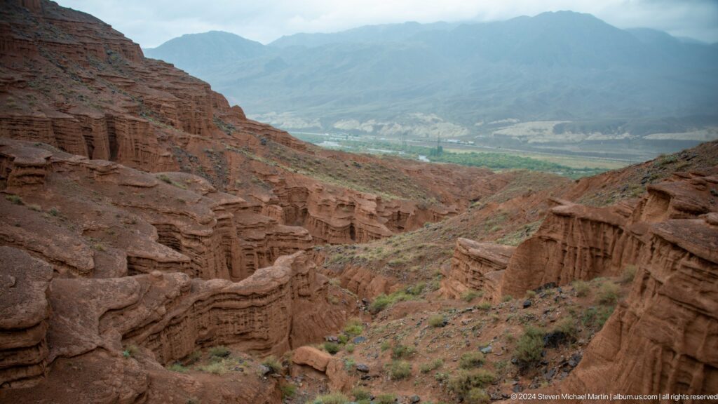 High overlook across red canyon toward green valley floor.