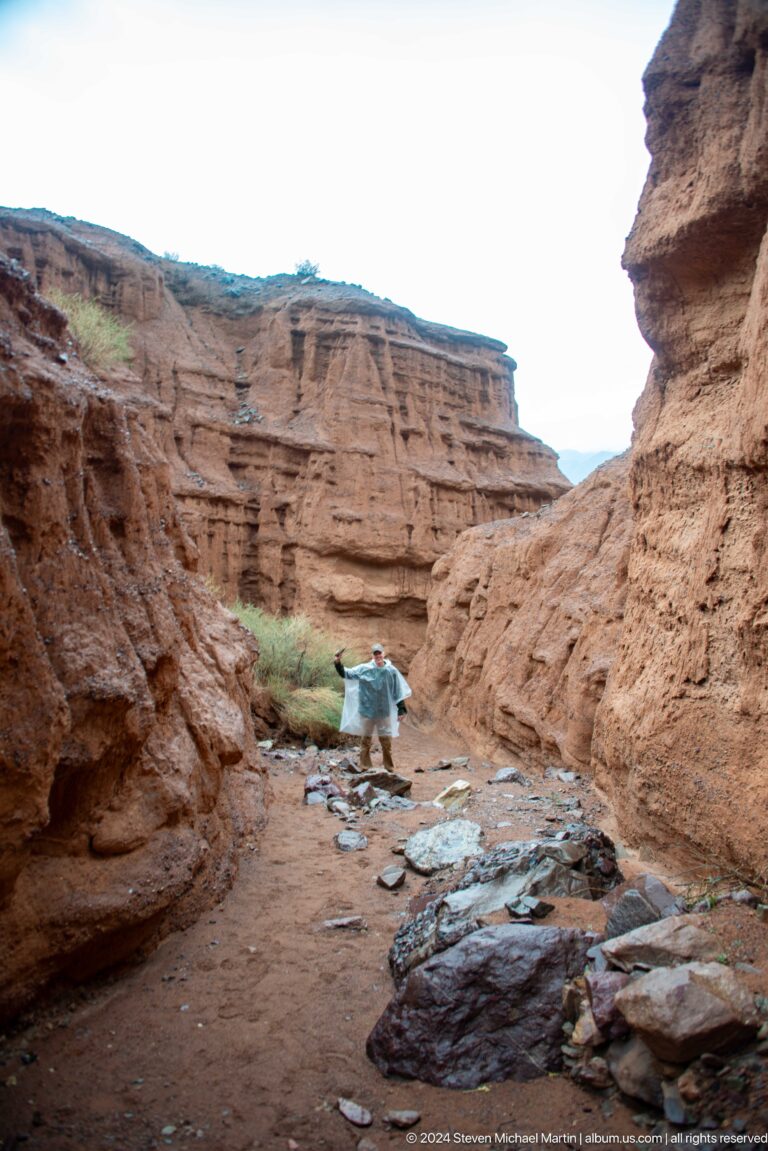 Visitor bending near stream in narrow canyon corridor.