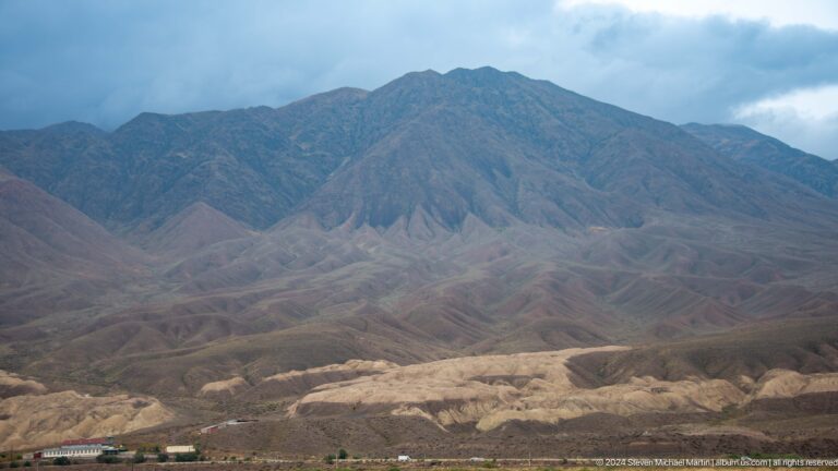 Broad mountain slope and pale valley floor under cloudy sky.