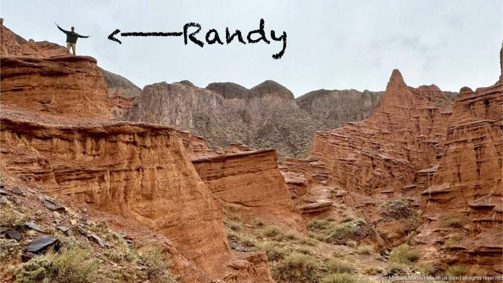 Wide red canyon scene with handwritten word near top.