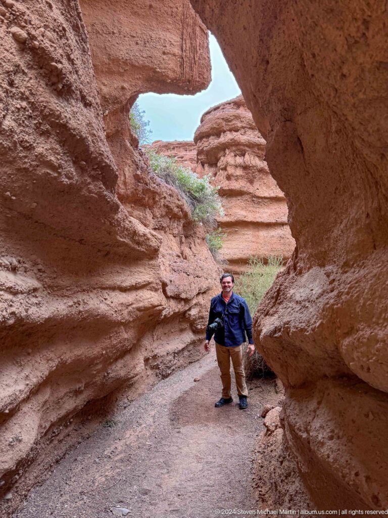 Man standing inside rounded canyon opening.