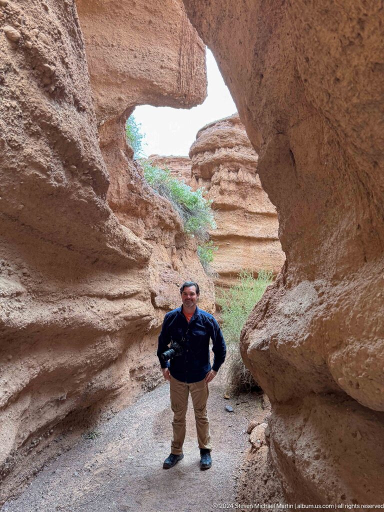 Man standing beneath curved overhanging canyon wall.