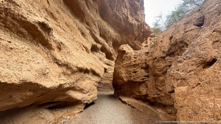 Shallow muddy stream flowing through narrow ochre canyon.