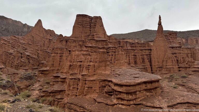 Broad frontal view of terraced red cliff and isolated spire.
