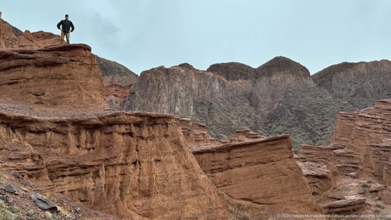 Red canyon ridge beneath gray scalloped mountains.