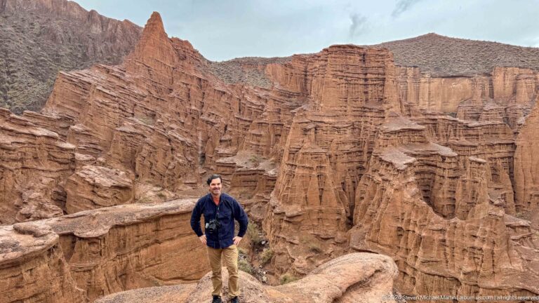 Visitor standing on overlook above deeply cut red canyon.