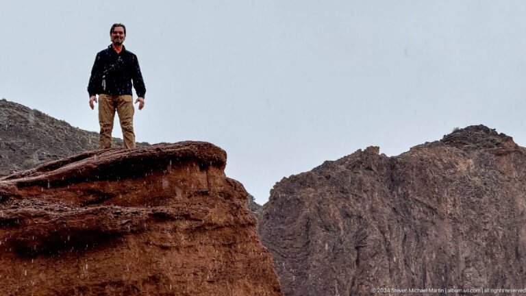 Visitor's lower legs standing on dark red ledge above canyon.