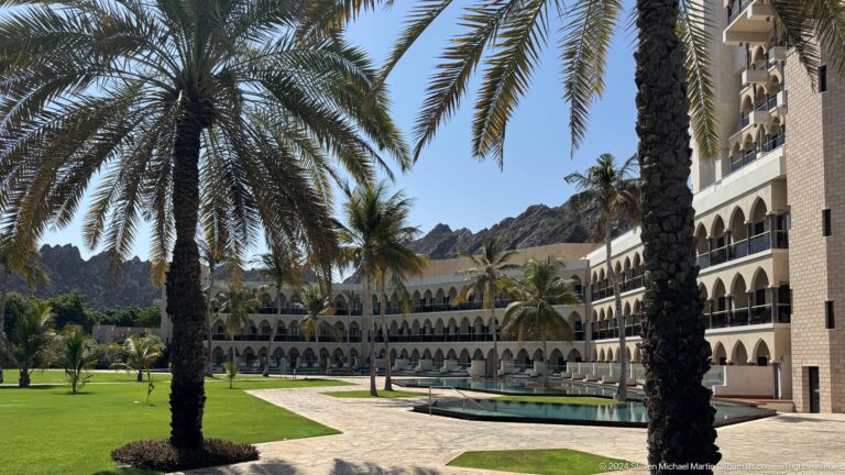 Resort courtyard lawn framed by palms and arcades in Muscat, Oman.