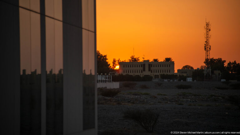 Silhouetted building and palms against orange sunset in Muscat, Oman.