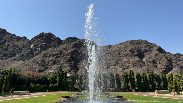 Fountain jet before rugged mountain cliff in Muscat, Oman.