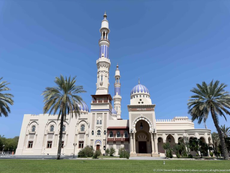 Ornate mosque facade and minaret among palms in Muscat, Oman.