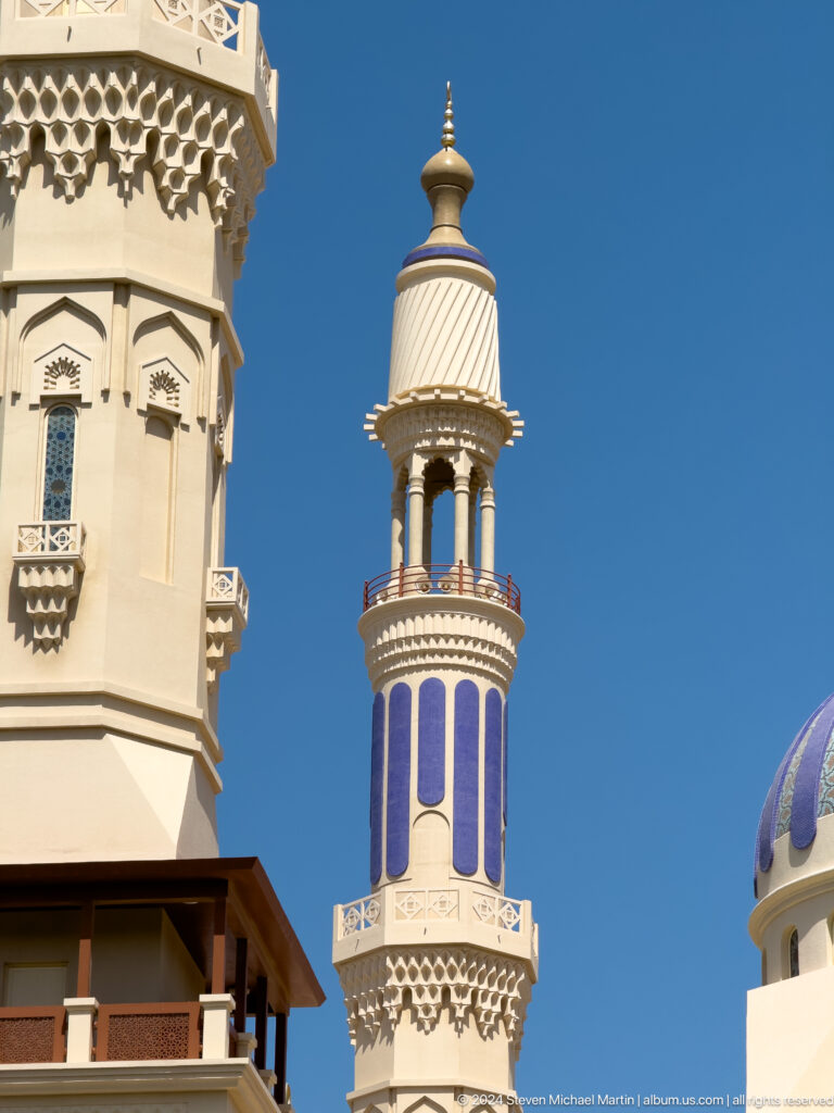 Striped minaret and pale tower against sky in Muscat, Oman.