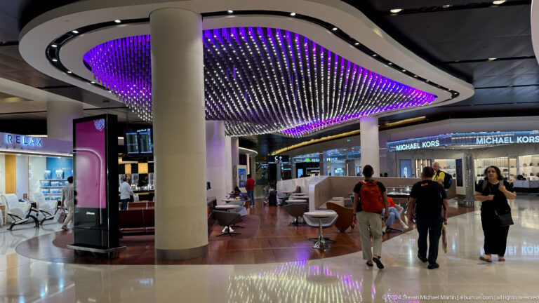 Airport concourse beneath purple illuminated ceiling in Muscat, Oman.