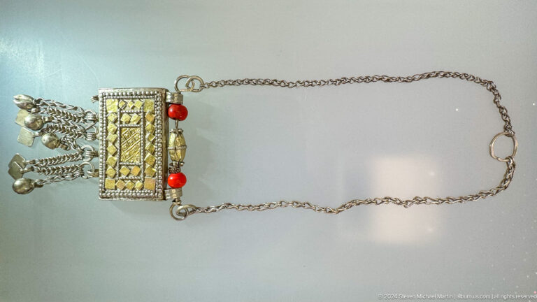 Rectangular pendant with red bead accents on chain in Muscat, Oman.