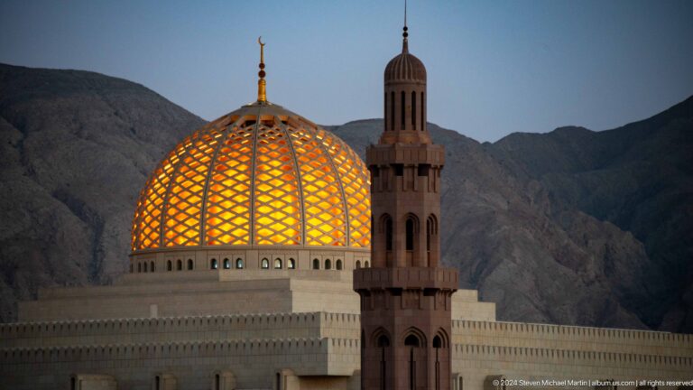 Golden dome behind dark minaret at dusk in Muscat, Oman.