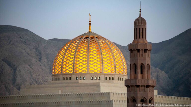 Golden dome and minaret against mountain slope in Muscat, Oman.