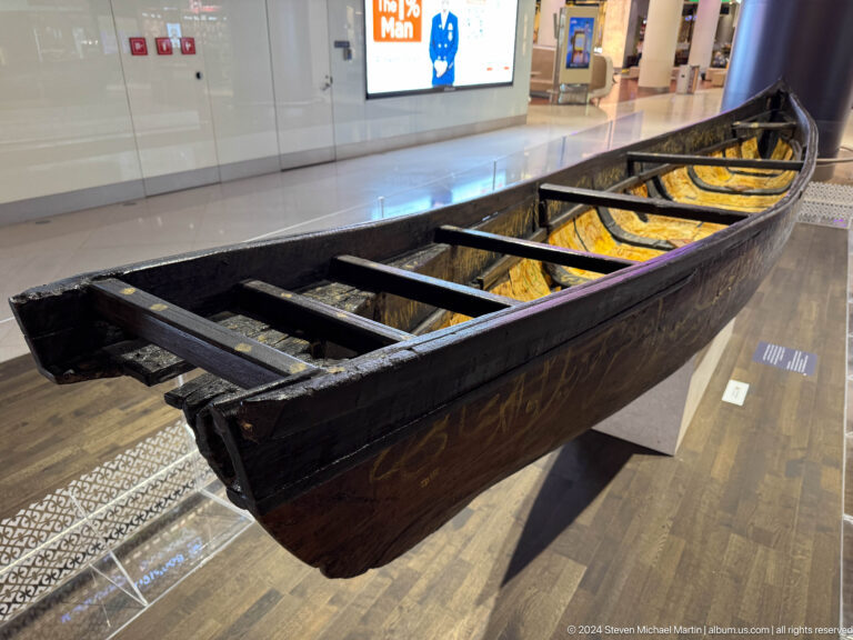 Dark wooden traditional boat displayed indoors in Muscat, Oman.