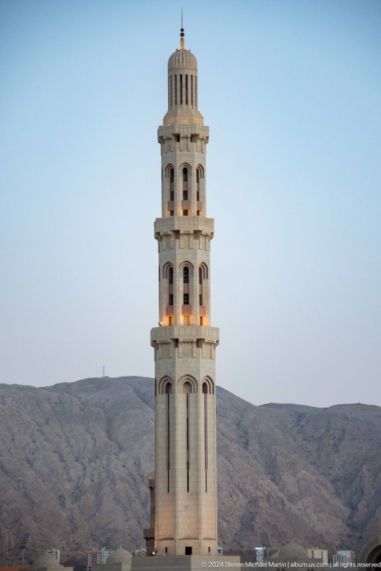Isolated tall minaret against pale sky and mountains in Muscat, Oman.