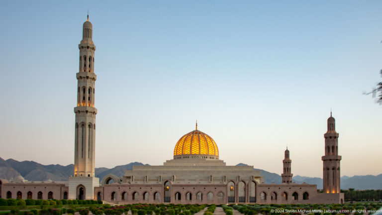 Wide mosque with central golden dome and paired minarets in Muscat, Oman.