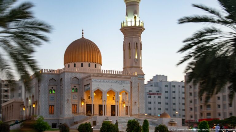 White mosque with golden dome and minaret at dusk in Muscat, Oman.