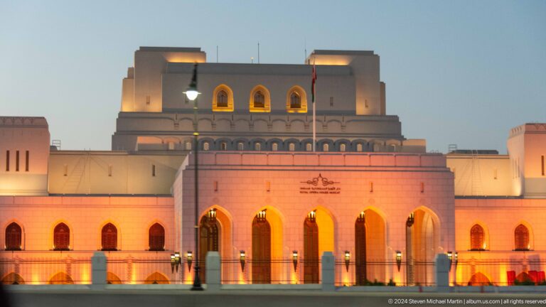 Orange-lit monumental facade with central arch in Muscat, Oman.