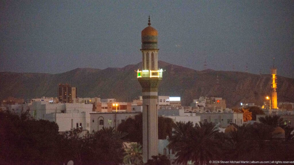 Minaret illuminated at night against mountains in Muscat, Oman.