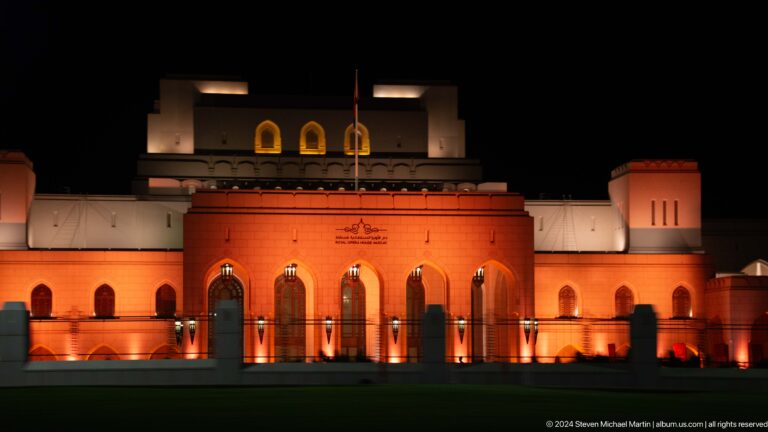 Royal Opera House facade illuminated amber at night in Muscat, Oman.