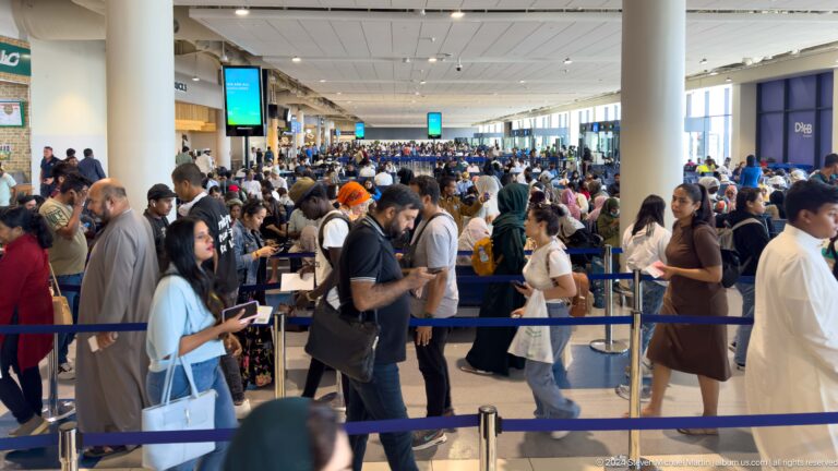 Crowded airport check-in hall with queue barriers in Muscat, Oman.