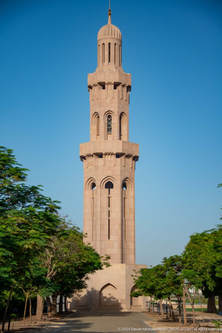 Sand-colored minaret rising above trees in Muscat, Oman.