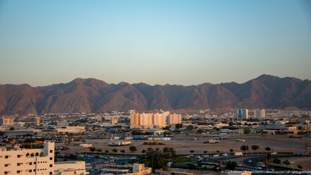 Broad Muscat skyline at sunset beneath mountains in Muscat, Oman.