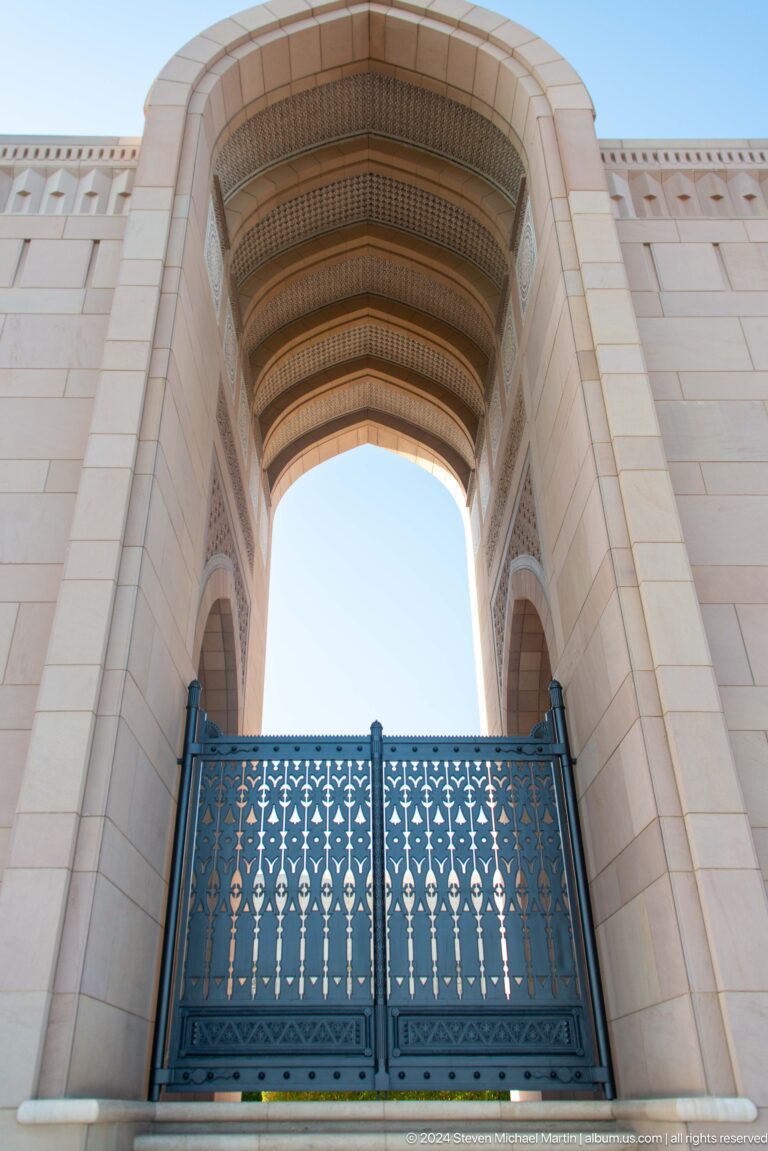 Tall pointed arch framing blue balcony screen in Muscat, Oman.