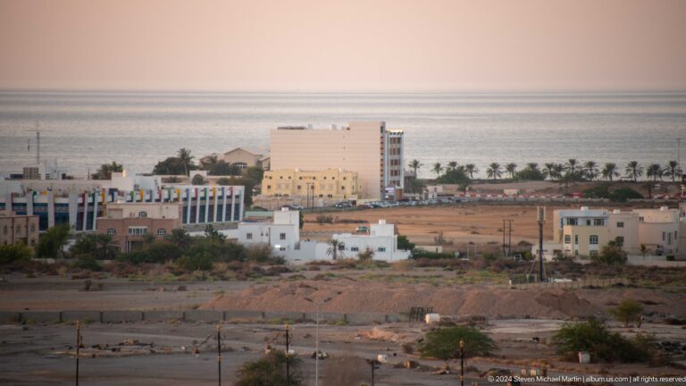 Large pale institutional building beyond open ground in Muscat, Oman.