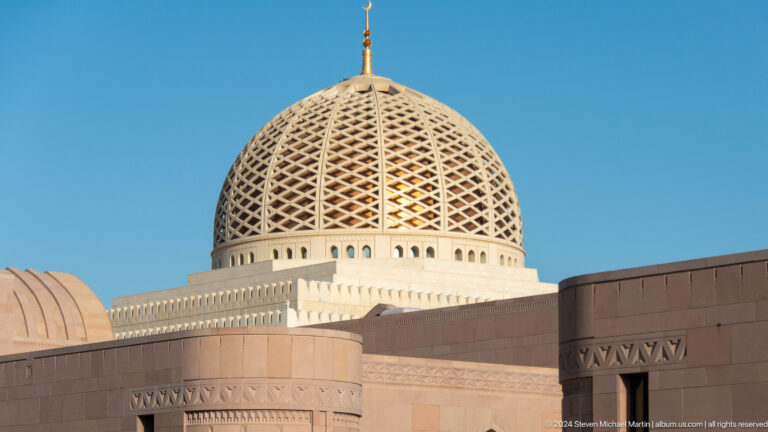Patterned dome rising above warm stone wall in Muscat, Oman.