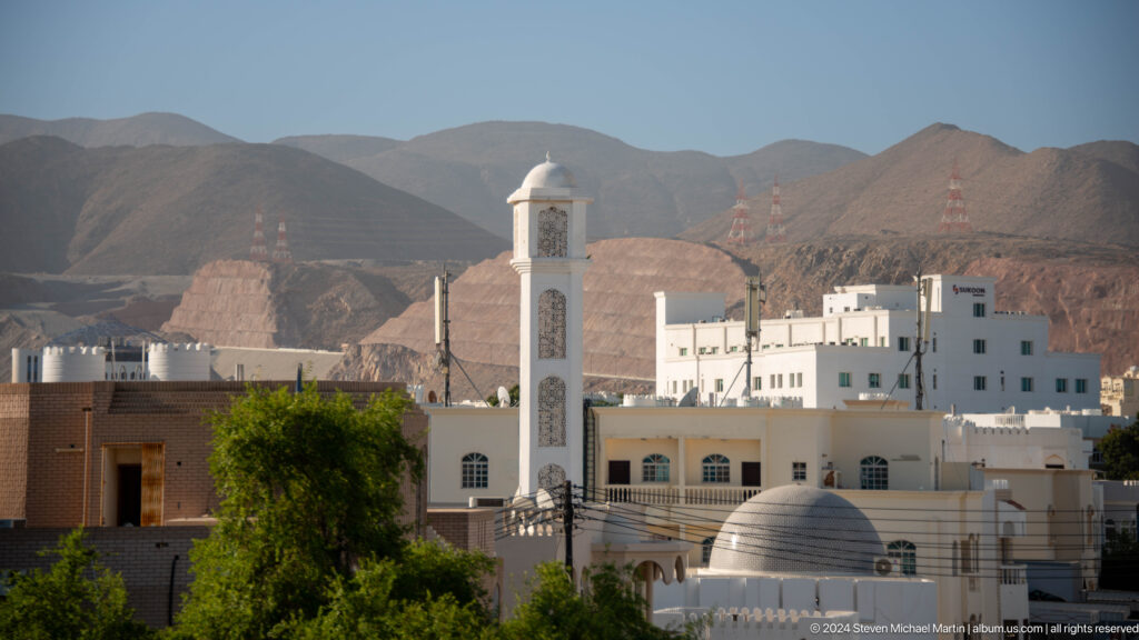 White mosque and minaret among low buildings and mountains in Muscat, Oman.
