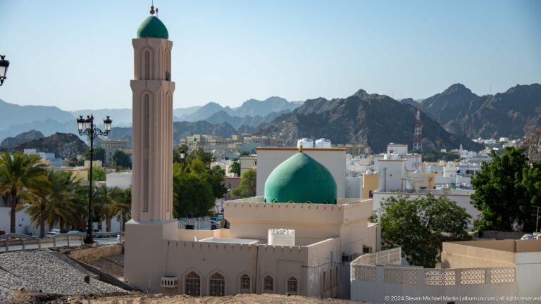 Turquoise dome and pale minaret in urban valley in Muscat, Oman.