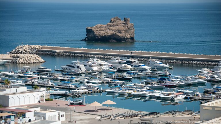 Marina filled with white yachts and rocky islet beyond in Muscat, Oman.