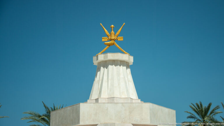 Gold Omani emblem atop white monument in Muscat, Oman.