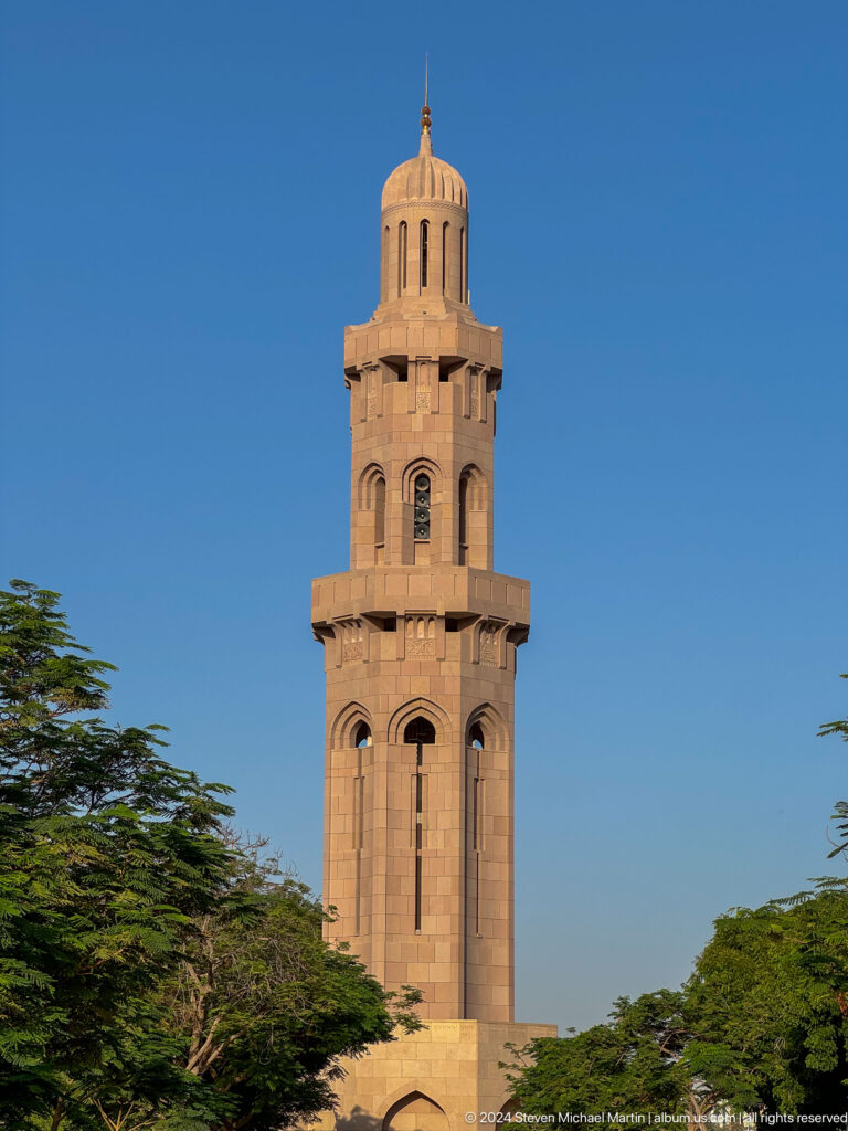 Sand-colored minaret framed by foliage in Muscat, Oman.