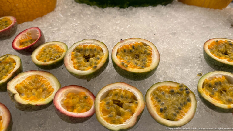 Halved passion fruits on crushed ice with exposed yellow-orange pulp and black seeds.