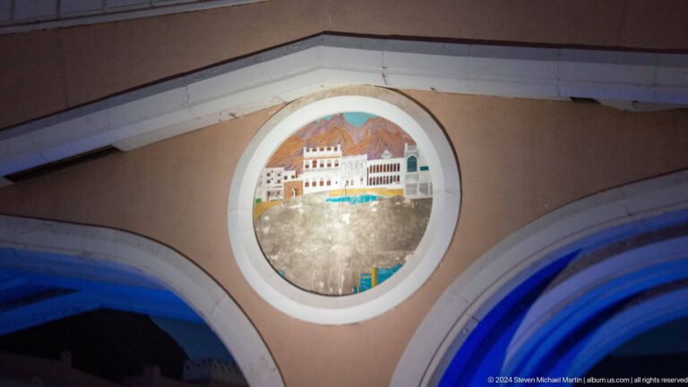 Round illuminated mutrah emblem mounted above an arch.