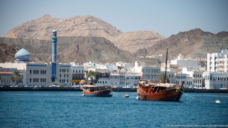 Two wooden dhows crossing blue harbor water.