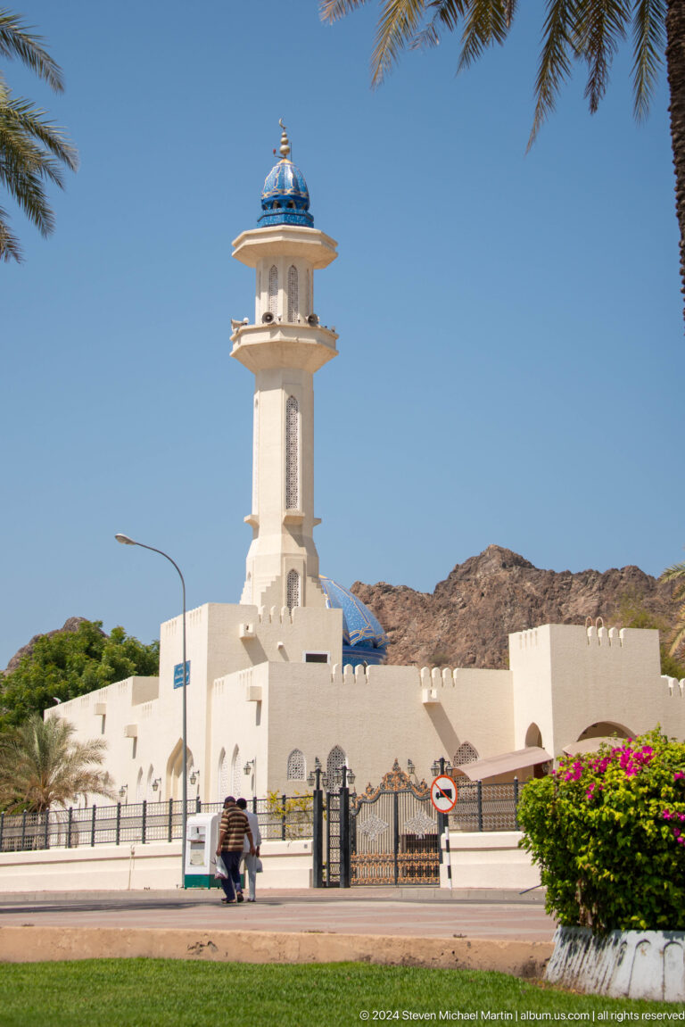 White mosque minaret against mountain ridge.