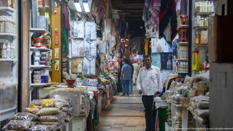 Narrow bazaar aisle lined with merchandise and shoppers.