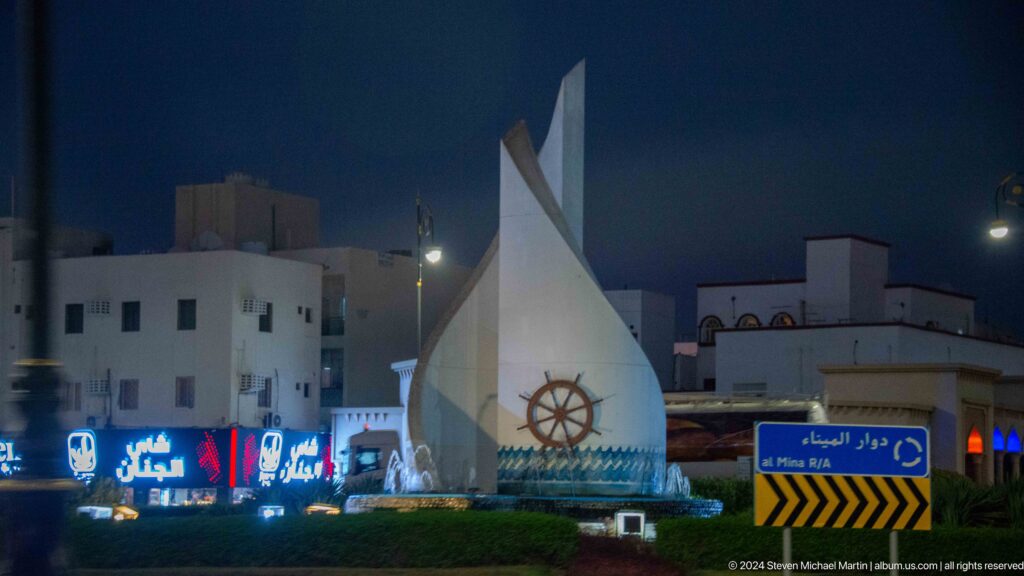 White roadside monument with ship's wheel motif at night.