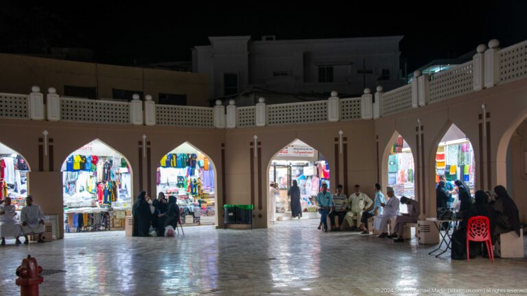 Night arcade with illuminated shopfronts and pedestrians.