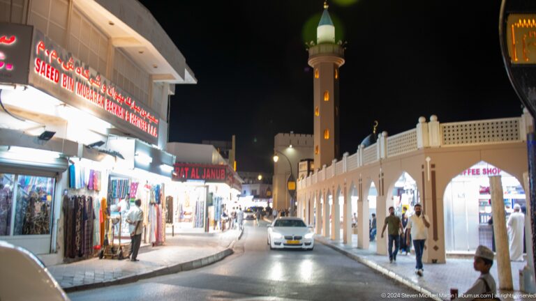 Busy market street with minaret and shops at night.
