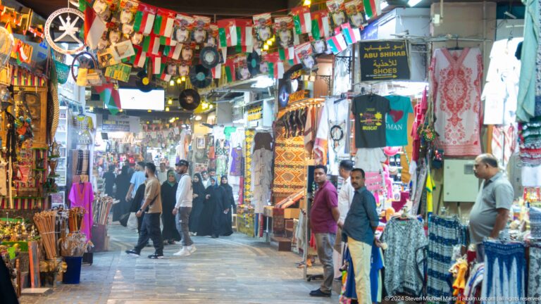 Crowded souq aisle with hanging textiles and souvenirs.