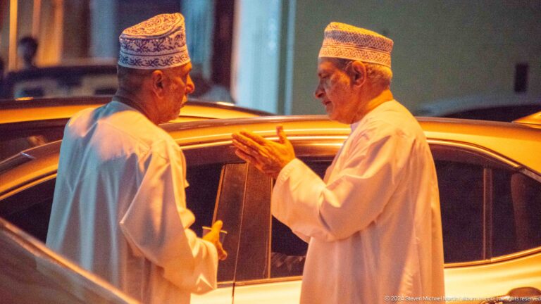 Two omani men in white dishdashas talking beside a car.