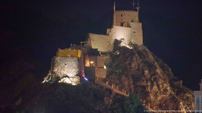 Mutrah fort illuminated on rocky hill at night.